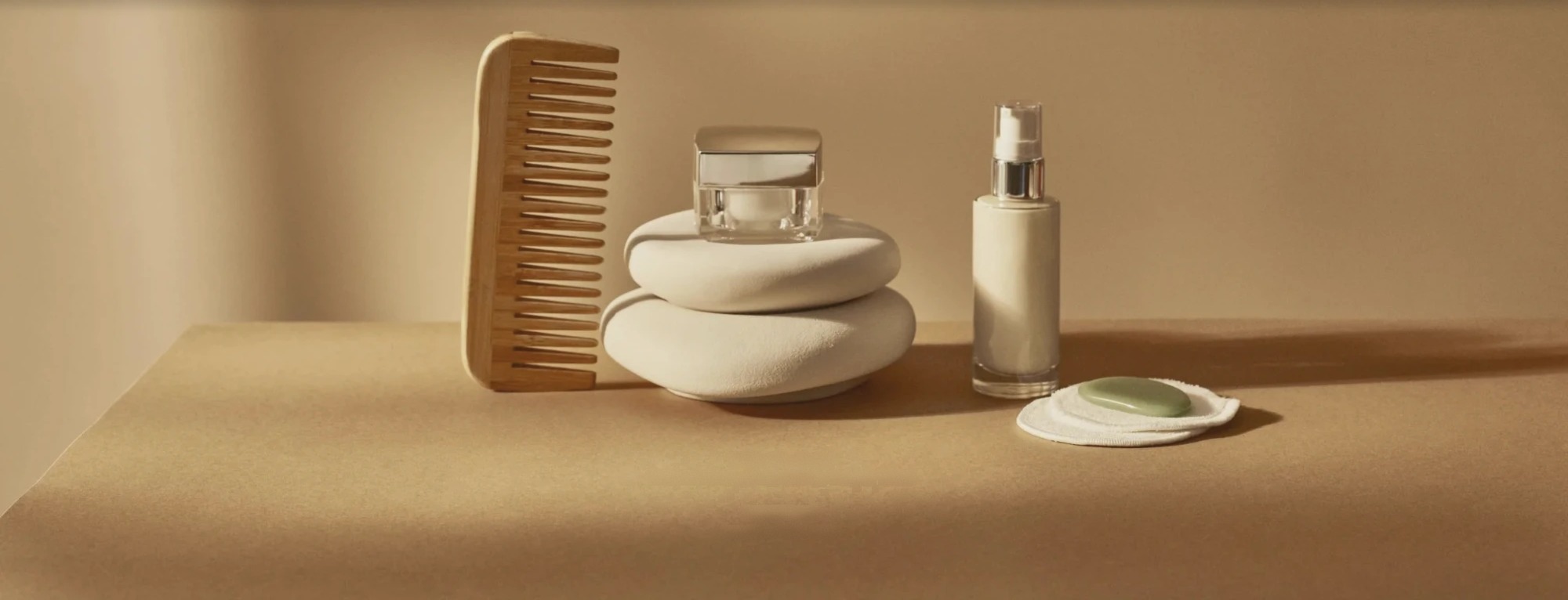 A wooden comb, stacked stones and glass bottles on a sand-colored table in warm afternoon light